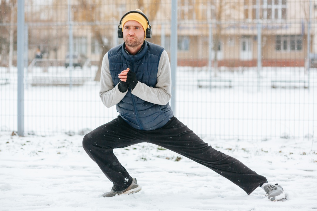 This active young man is seen embracing wintertime for his athletic pursuits, performing gymnastics and staying healthy with headphones.