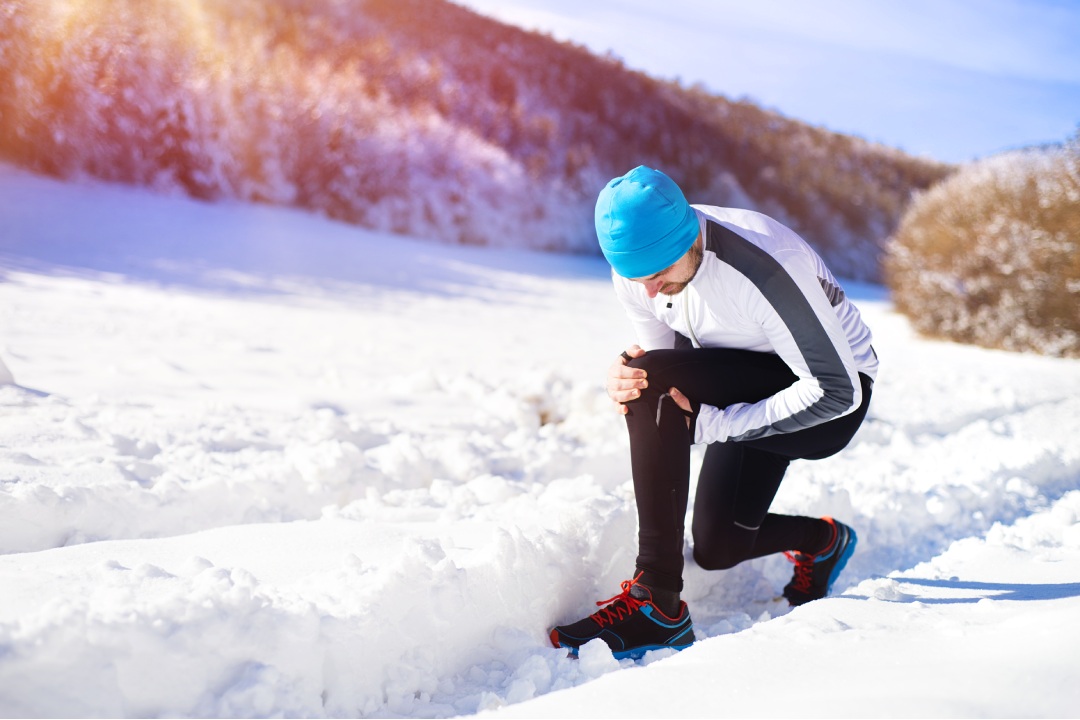 Injury of a young sportsman jogging outside in sunny winter park